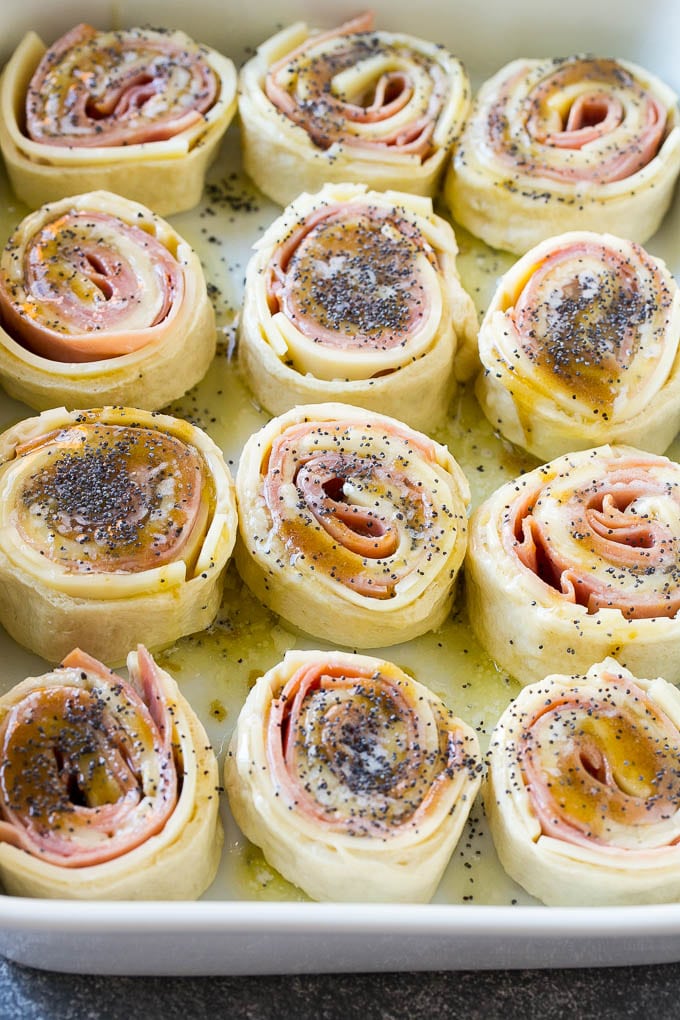 Dough rolled up with ham and cheese and topped with a poppy seed butter in a ceramic dish.