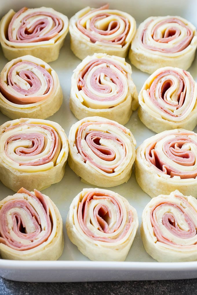 Rolled up ham, cheese and pizza dough circles in a baking dish.