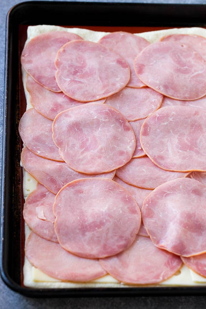 Spread ham and cheese onto a sheet of pizza dough, then roll up and bake.