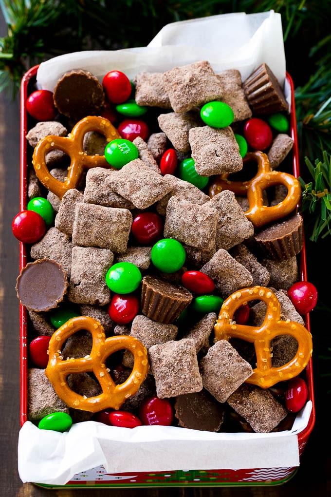 A tin of reindeer chow with chocolate coated chex, M&M's and pretzels.