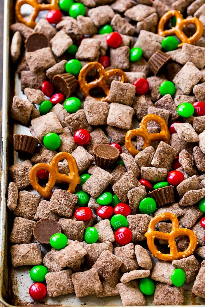 A sheet pan of Christmas muddy buddies mixed with candy and peanut butter cups.