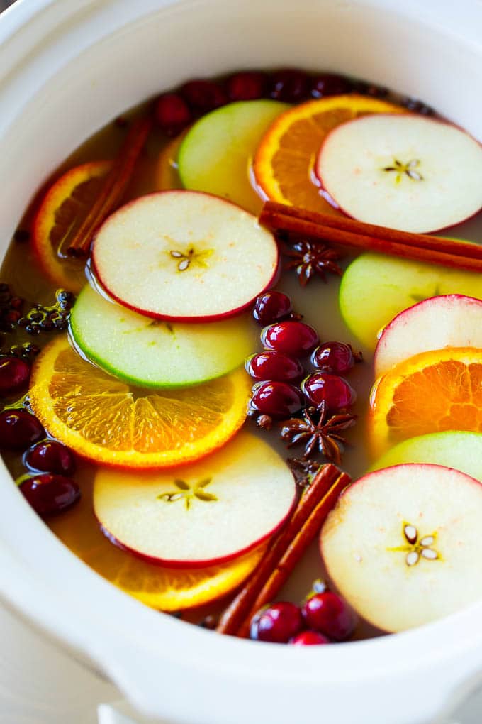 Slow cooker apple cider with oranges, apple slices, cinnamon sticks and cranberries.