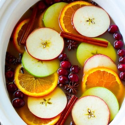 Slow cooker apple cider garnished with apple slices, oranges, cranberries, cinnamon sticks and spices.