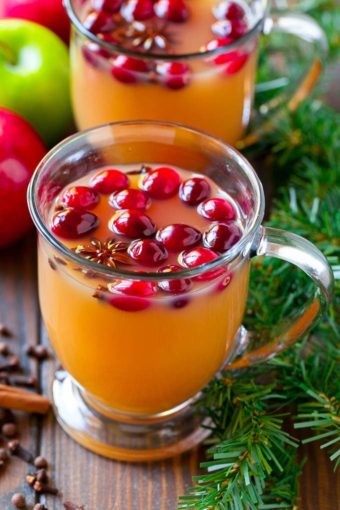 Mugs of slow cooker apple cider garnished with cranberries.