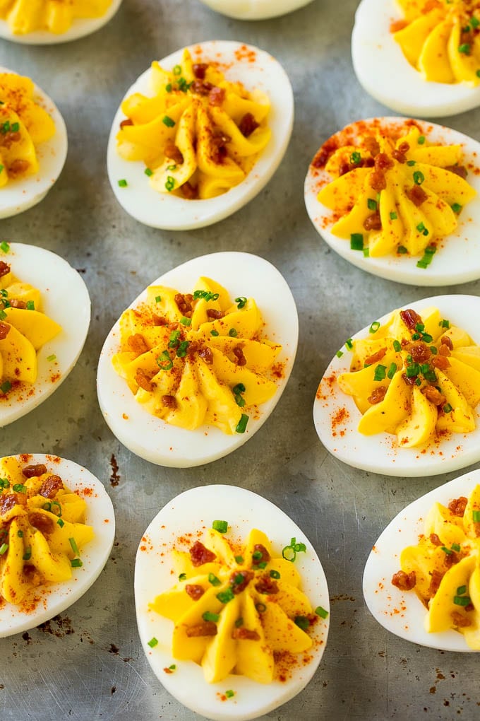 Bacon deviled eggs topped with chives and paprika on a sheet pan.