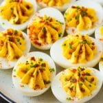 A plate of bacon deviled eggs garnished with sliced chives and smoked paprika.