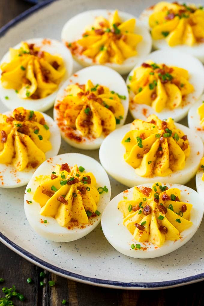 A plate of bacon deviled eggs garnished with sliced chives and smoked paprika.