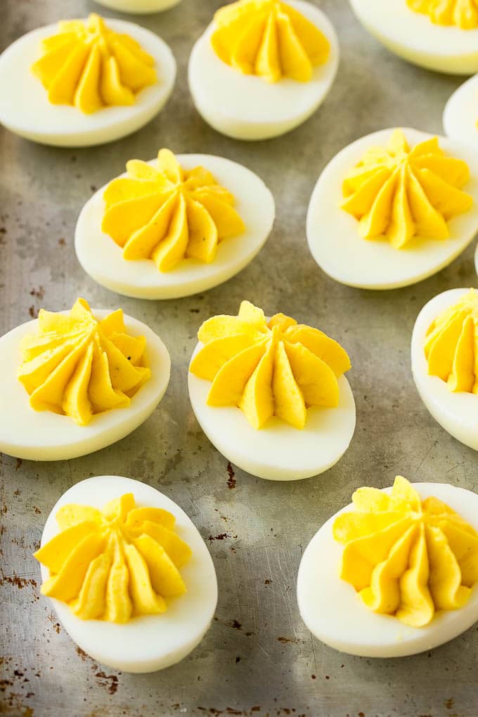 Deviled eggs with a decoratively piped filling on a sheet pan.