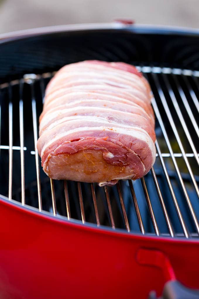 A bacon wrapped pork loin on a Weber kettle grill.