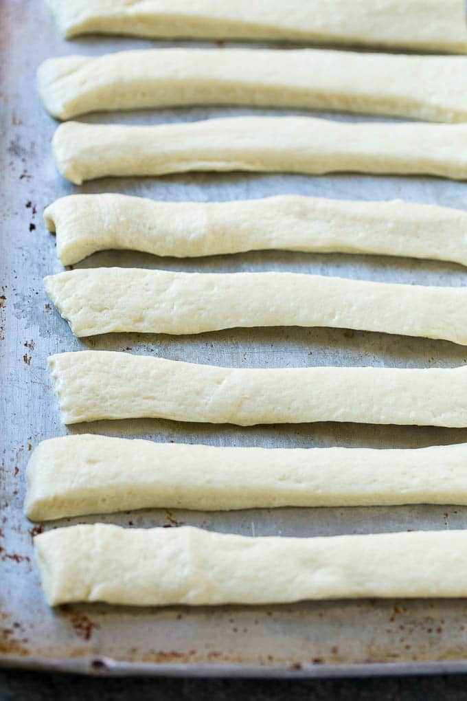 Strips of pizza dough on a sheet pan that are ready to be tied up.