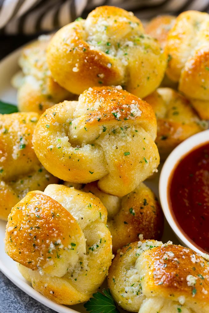 A plate of garlic knots slathered in butter next to a cup of marinara sauce. 