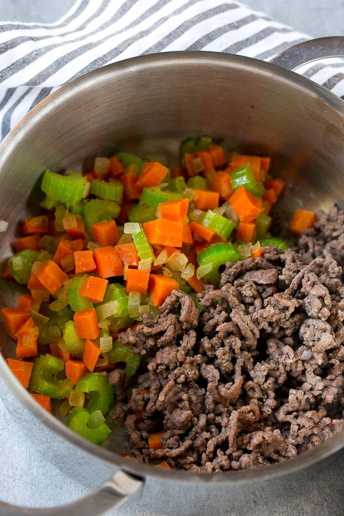 Ground beef is added to the vegetables in a pot.