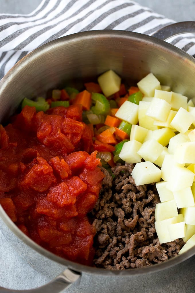 Potatoes and tomatoes go into hamburger soup before the pot comes to a simmer.