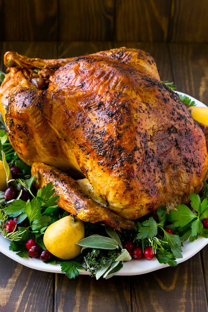 A whole herb roasted turkey surrounded by herbs and fruit.