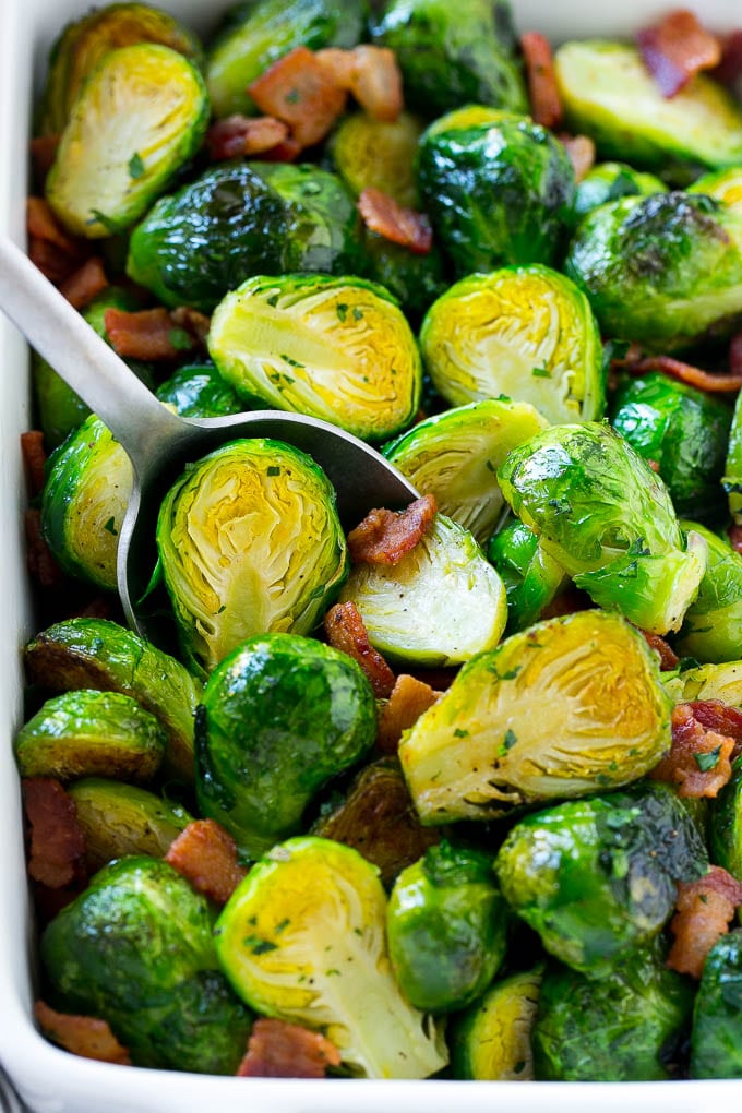 A serving dish full of roasted brussels sprouts with bacon and parsley.