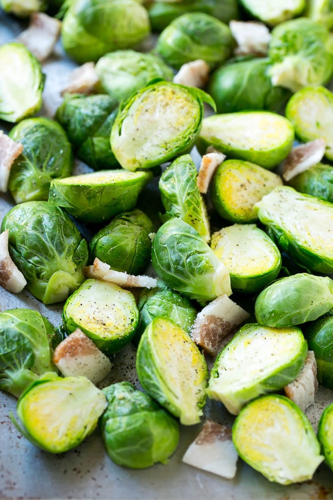 Raw halved brussels sprouts with uncooked bacon on a sheet pan.