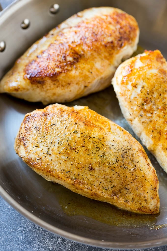 Seared chicken breasts in a pan for baked lemon chicken.