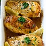 A baking dish full of lemon chicken coated in sauce and garnished with lemons and parsley.