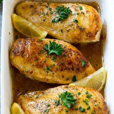 A baking dish full of lemon chicken coated in sauce and garnished with lemons and parsley.
