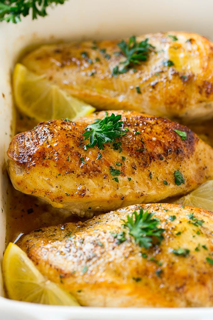 Baked lemon chicken in a white dish topped with herbs.