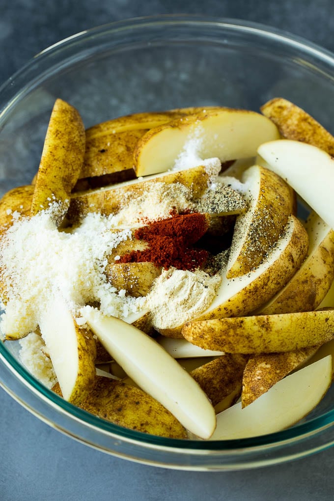 Sliced potatoes in a bowl with a variety of seasonings.