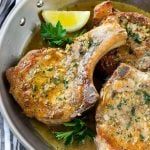 Brown sugar pork chops with garlic, butter and herbs in a frying pan.