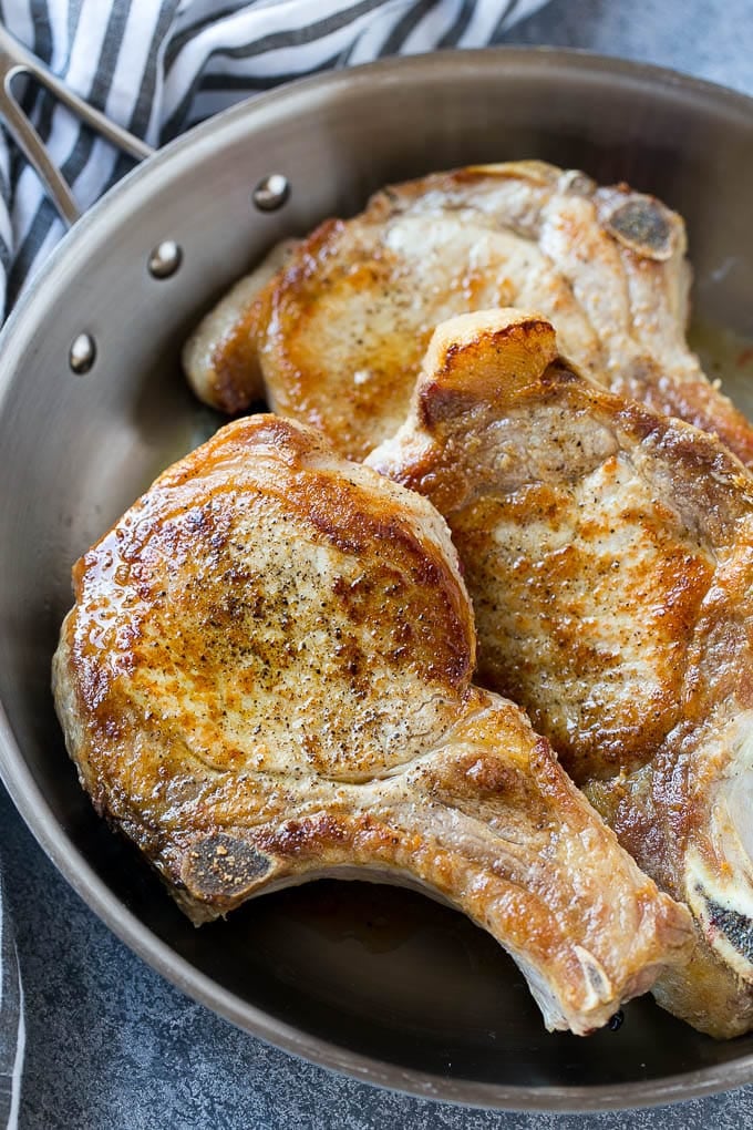 Browned bone in pork chops in a frying pan.