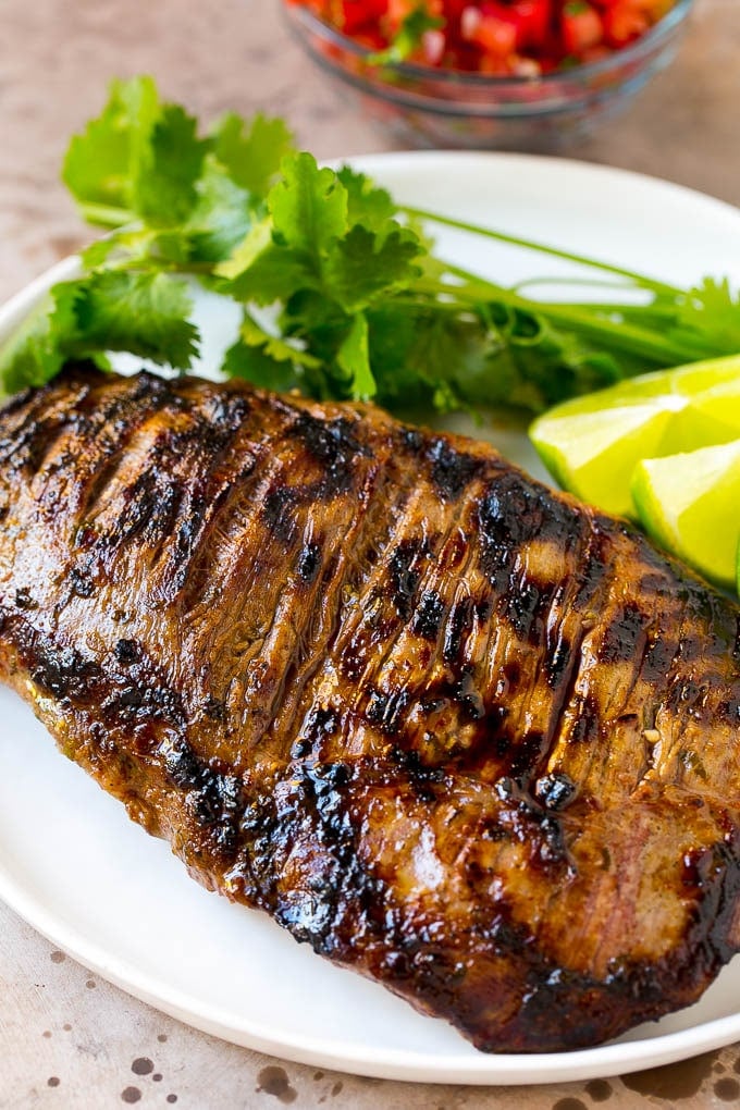 Grilled carne asada steak garnished with cilantro and limes.