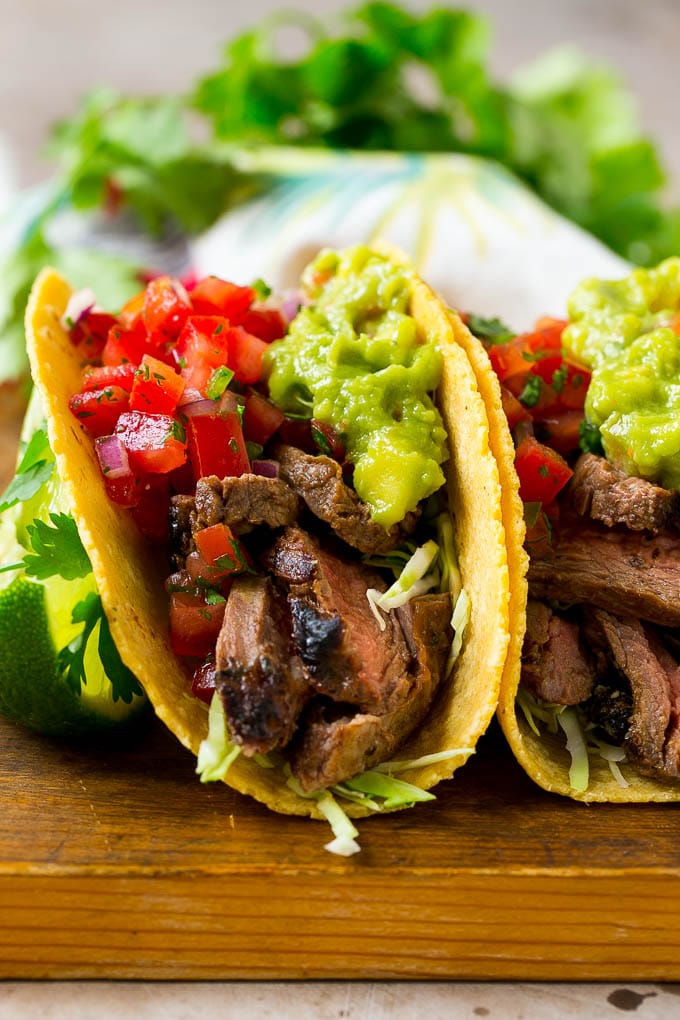 Carne asada tacos in corn tortillas, topped with salsa and guacamole.