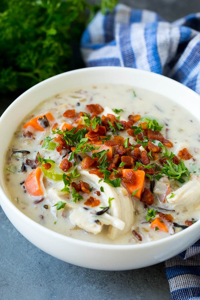 A bowl of chicken and wild rice soup topped with bacon and parsley.