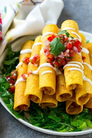A stack of chicken taquitos with a drizzle of sour cream and pico de gallo topping.