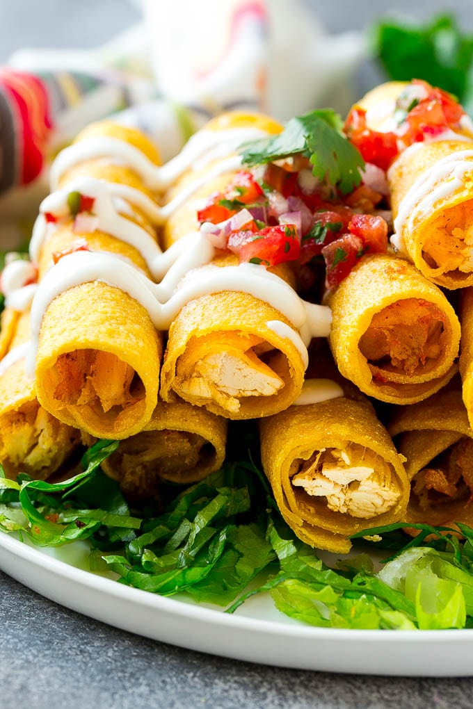 A plate of chicken taquitos on a bed of lettuce, topped with sour cream and pico de gallo.