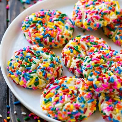 A plate of funfetti cookies coverd in rainbow sprinkles.