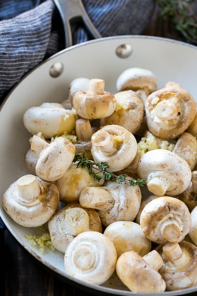 Uncooked button mushrooms with herbs, garlic and butter in a frying pan.