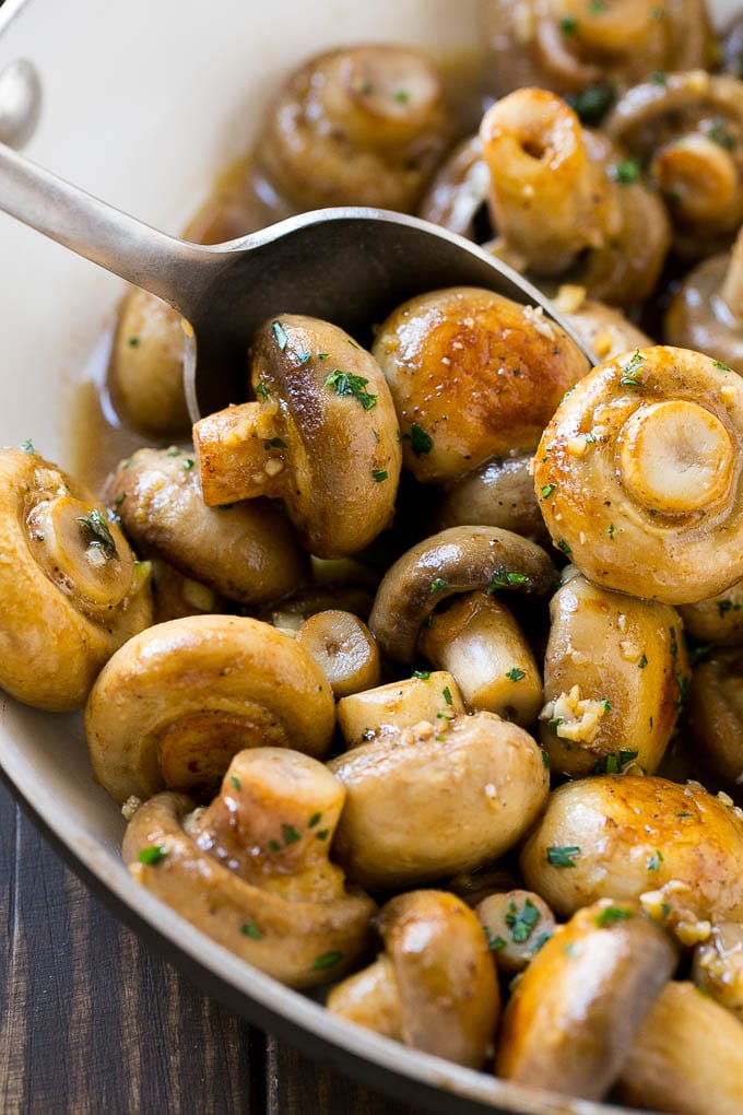 A pan of sauteed garlic mushrooms with a serving spoon.