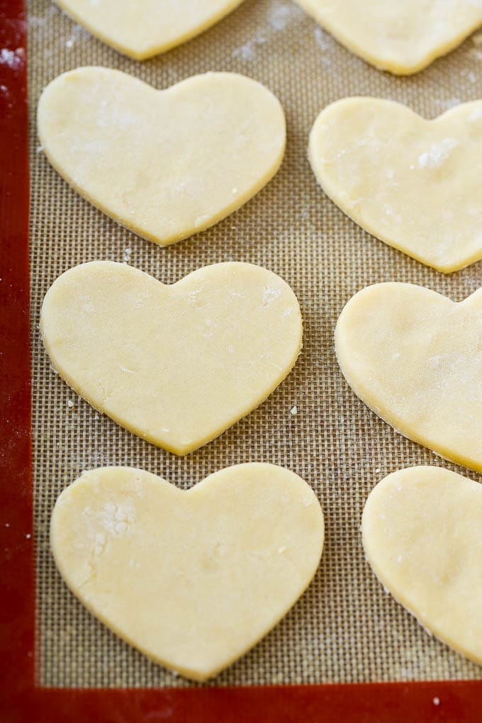Heart shaped sugar cookie dough pieces on a baking mat.