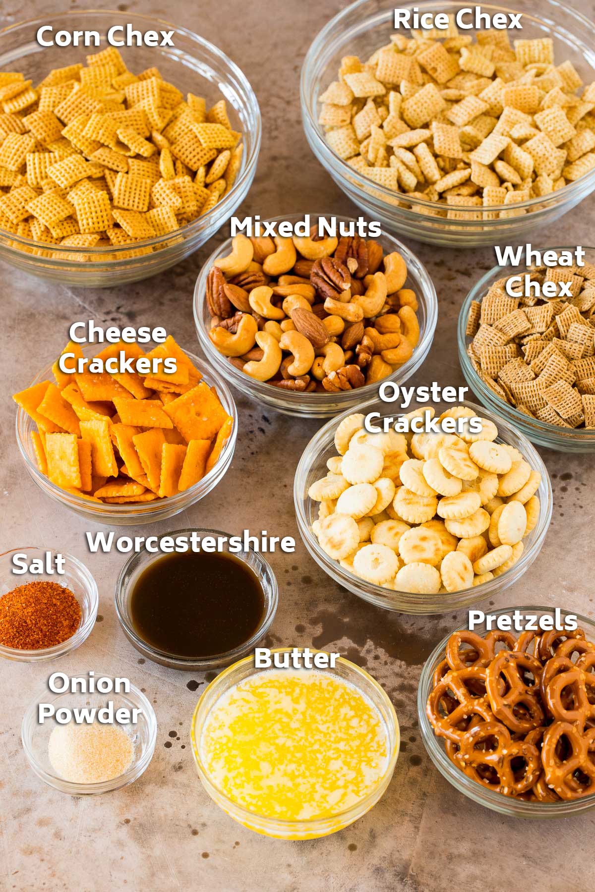 Bowls of ingredients including cereal, crackers, pretzels, nuts, butter and seasonings.