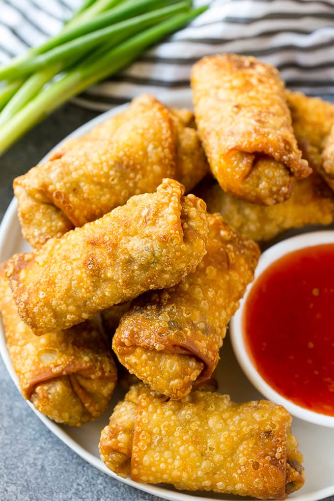A pile of fried homemade egg rolls with dipping sauce.