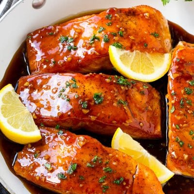 A pan of honey garlic salmon topped with a savory sauce and garnished with parsley and lemon.
