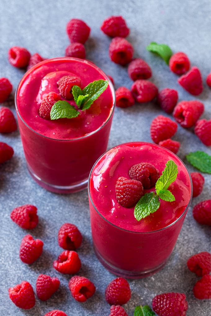 Two raspberry smoothies with a garnish of fresh mint and raspberries.