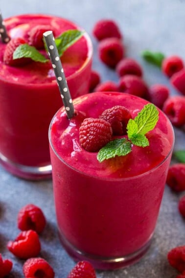 A raspberry smoothie garnished with mint and berries, with a straw.