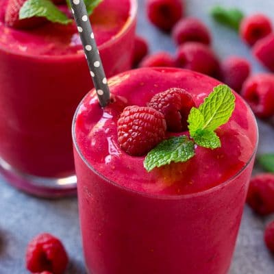 A raspberry smoothie garnished with mint and berries, with a straw.