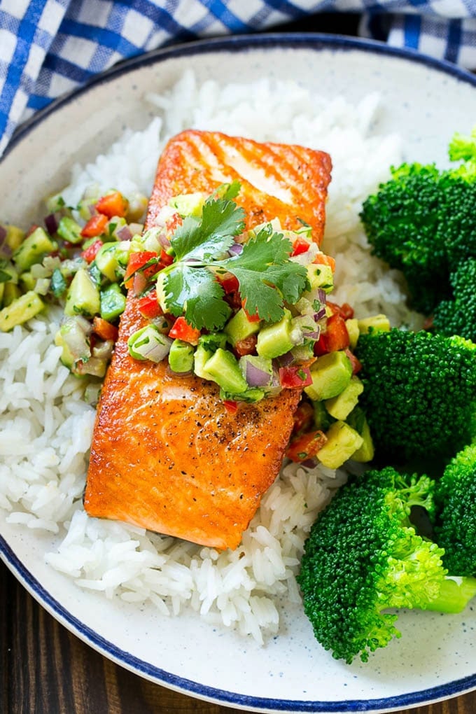 A salmon fillet with avocado salsa served over rice and broccoli.