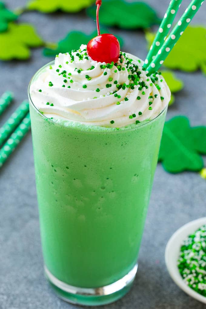 A glass of shamrock shake topped with whipped cream, sprinkles and a cherry.