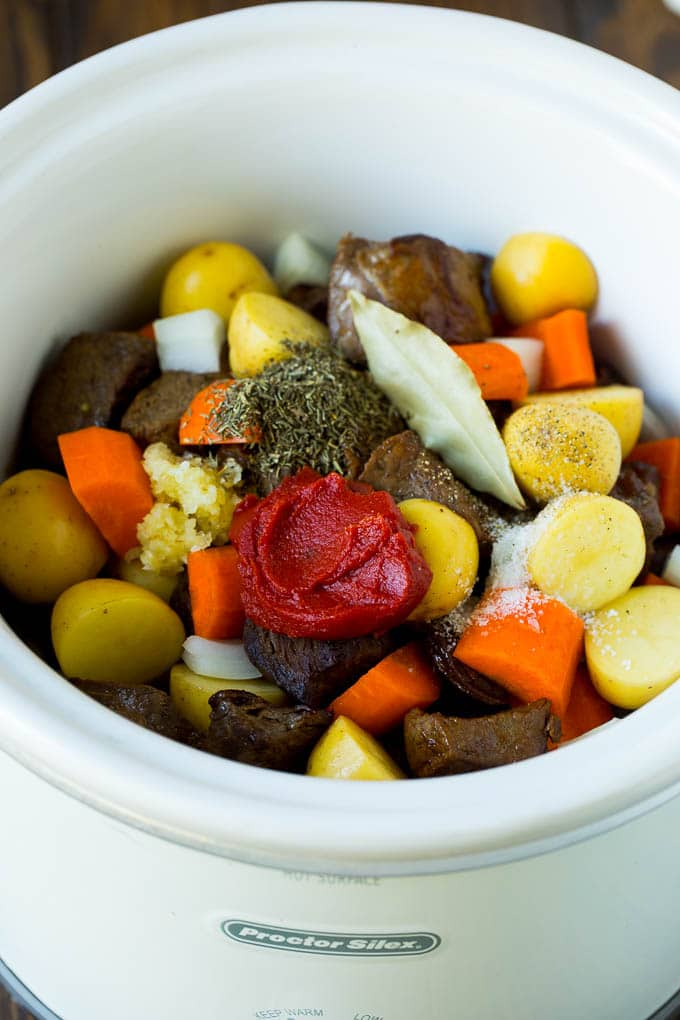 A crock pot filled with beef, vegetables, tomato paste, herbs and spices.