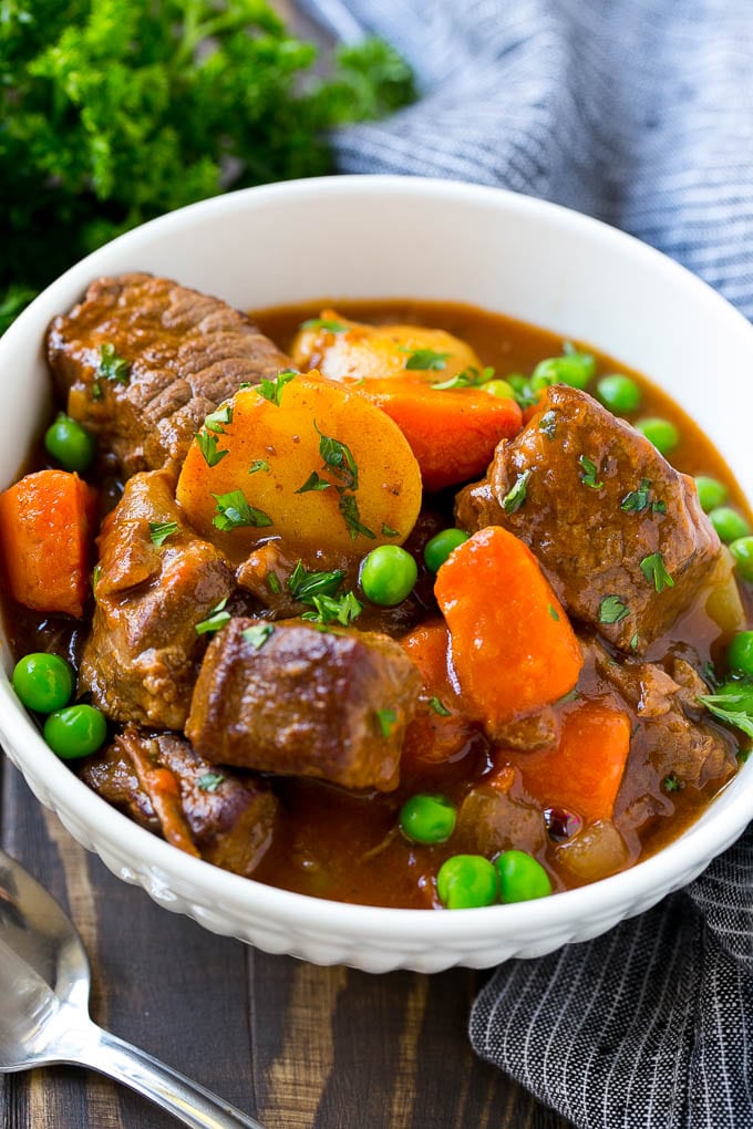 A bowl of slow cooker beef stew with meat, carrots, potatoes and peas.