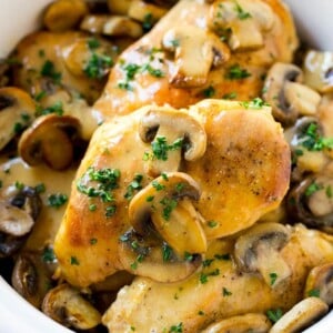 A slow cooker full of cooked chicken breasts topped with marsala wine and mushroom sauce.
