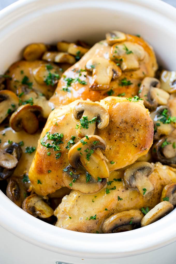 A slow cooker full of cooked chicken breasts topped with marsala wine and mushroom sauce.