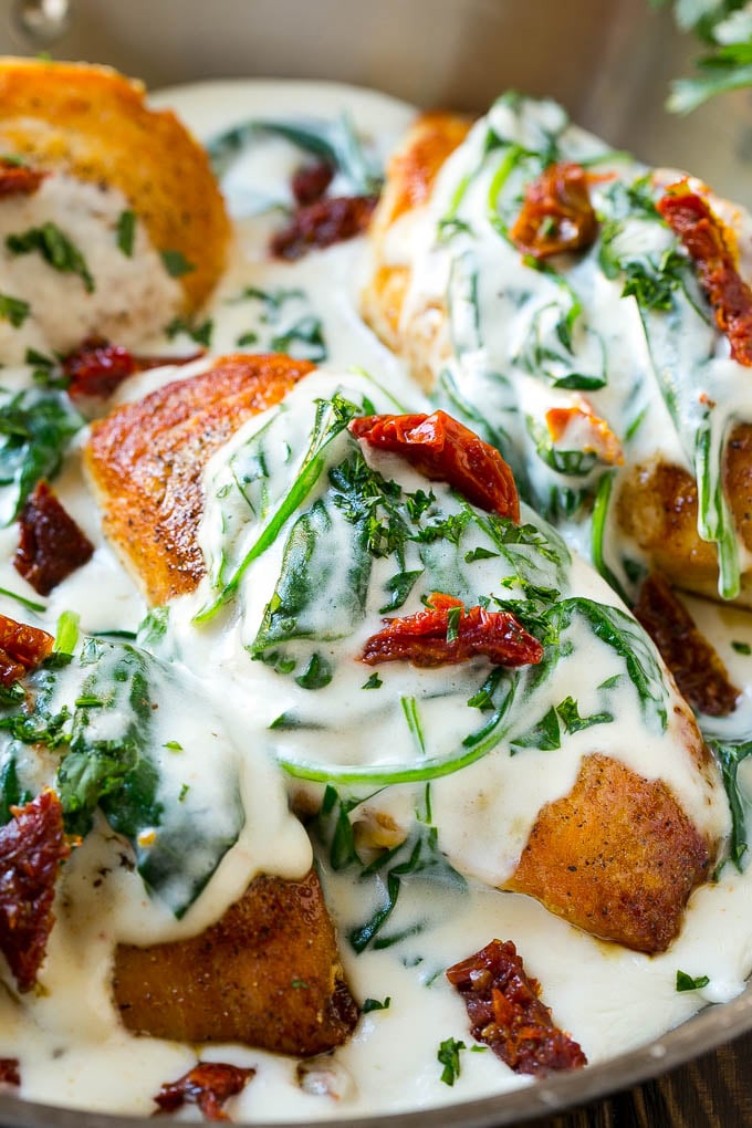 Golden brown chicken breasts topped with a creamy spinach and sun dried tomato sauce in a pan.