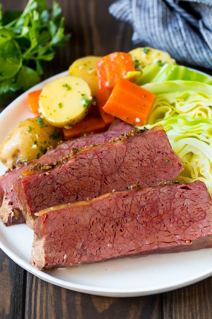 Sliced slow cooker corned beef on a plate with carrots, potatoes and cabbage.